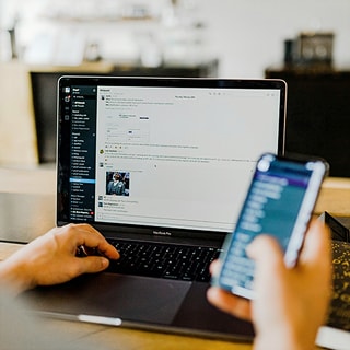 片手にスマートフォンを持ち、ノートパソコンの画面でメッセージやデータを確認する様子