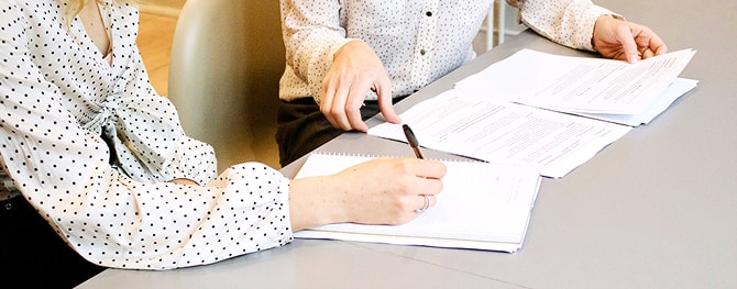 デスク上で資料を確認し、ペンで記入する2人の手元の様子