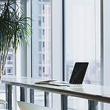 明るい窓際にノートパソコンが置かれたオフィスの風景