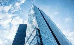 青空を背景に下から見上げたガラス張りの高層オフィスビル